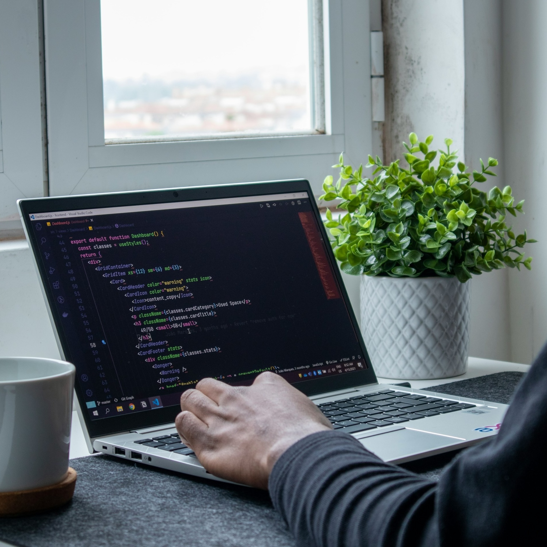 Developer coding on laptop with coffee and plant - professional development workspace